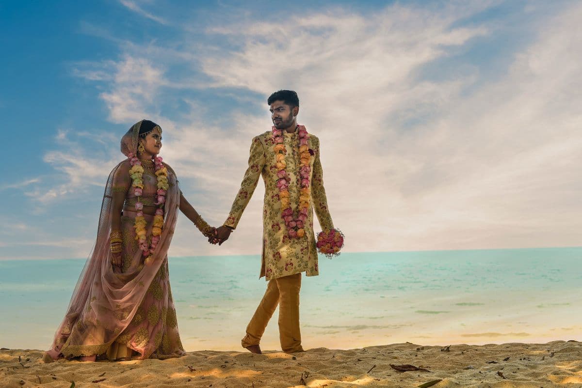 An Indian couple in wedding attire walking hand in hand